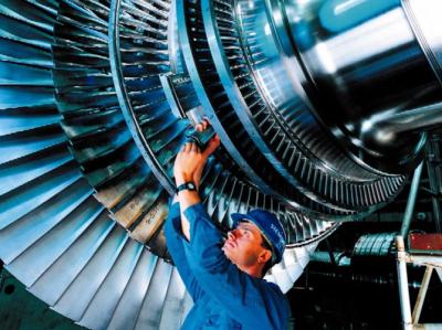 Fotoet viser et nærbillede af en dampturbine indefra. En mand i blå arbejdsskjorte og blå hjelm fra Siemens rækker armene op og justerer i det indvendige af en dampturbinen. 