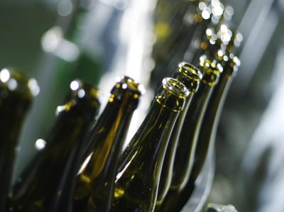 Fotoet viser en række tomme mørkegrønne ølflasker uden etiket og kapsel, som kører tæt på række gennem et tappeanlæg. 