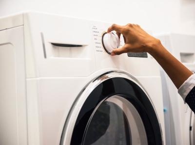Fotoet viser en persons hånd, der stiller på vaskeknappen på en vaskemaskine.